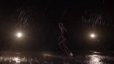 Sensual Young Woman Dancer Performing in the Rain in Dark Studio Against Black Backdrop and with Spotlights On. Water Drops Falling on the Floor Imitating Rain Shower. Dolly In and Out Shot