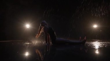 Sensual Young Woman Dancer Performing in the Rain in Dark Studio Against Black Backdrop and with Spotlights On. Water Drops Falling on the Floor Imitating Rain Shower