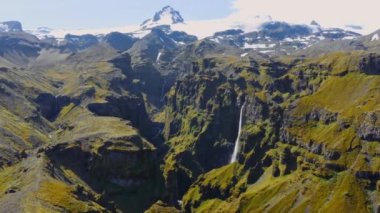 Arka planda, Şelaleli Mulagljufur Kanyonu ve Karlı Dağlar 'ın Görkemli Manzarası. Güney İzlanda 'nın eşsiz doğası. Panoramik çekim. Kamera Yakınlaştır