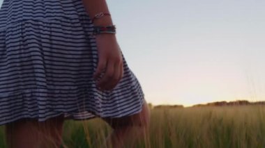 Yavaş çekim, gün batımında tarlada yürüyen çizgili elbiseli kadının yakın çekim görüntüsü.