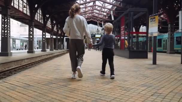 列車のホームに沿って歩く兄の手を握っている妹の広い追跡スローモーションショット — ストック動画