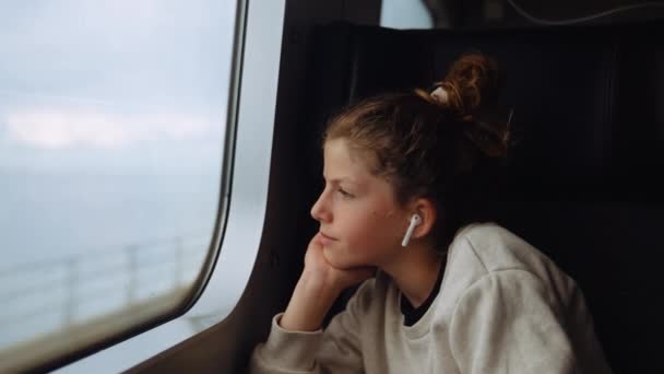 Medium Handheld Shot Young Girl Earbuds Sitting Train Looking Out — Stock Video