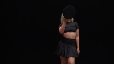 Siyah Arkaplan Karşıtı Profesyonel Dansçı. Uzun Sarı Saçlı Baştan Çıkarıcı Genç Kadın, Stüdyoların Sahnesinde Şapka Takıyor ve Kameraya Bakıyor. Çekim Dolly