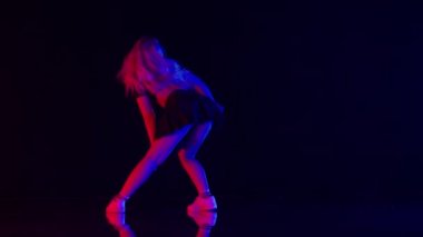 Uzun Sarı Saçlı Seksi Genç Kadın Renkli Sahne Işıkları Stüdyosunda Dans Ediyor. Karanlık Arkaplan 'a Karşı Güzel Performans ve Yerde Yansımalar. Yavaş Hareket Görüntüyü Büyüt