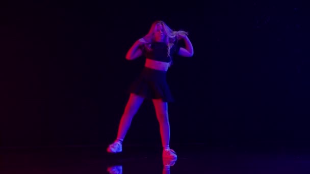 スタジオのカラフルなステージライトでロングブロンドの髪のダンスとセクシーな若い女性 暗い背景と床の反射に対する美しいパフォーマンス スローモーションショット — ストック動画