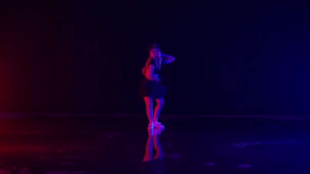 警察官のセクシーな若い女性スタジオのカラフルなステージライトで帽子ダンス 暗い背景と床の反射に対する美しいパフォーマンス スローモーションショット — ストック動画