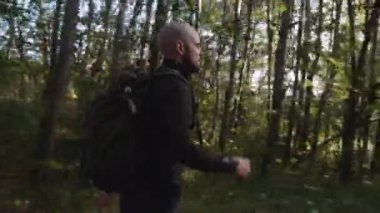 Ormandaki küçük patika boyunca sırt çantalı Kel Turist 'in yan görüntüsü. Kamera adamı takip ediyor. Orta Çekim