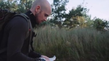 Ormanda Sırt çantalı Kel Turist Yürüyüşü. Ha 'nın elinde kağıt harita var. Kamera adamı takip ediyor. Orta Çekim