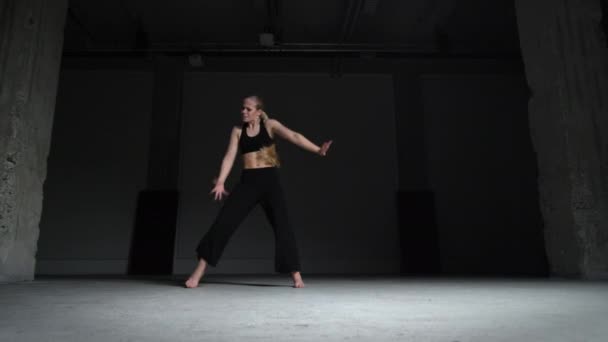 精力充沛的年轻女舞蹈家 金发碧眼 头戴黑色上衣 裤子与混凝土墙一起独自在工作室里跳舞 静态射击 — 图库视频影像