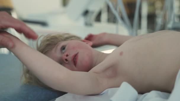 病院のベッドの上に寝そべっている少年の肖像 医者は腕に触れる スローモーションショット — ストック動画