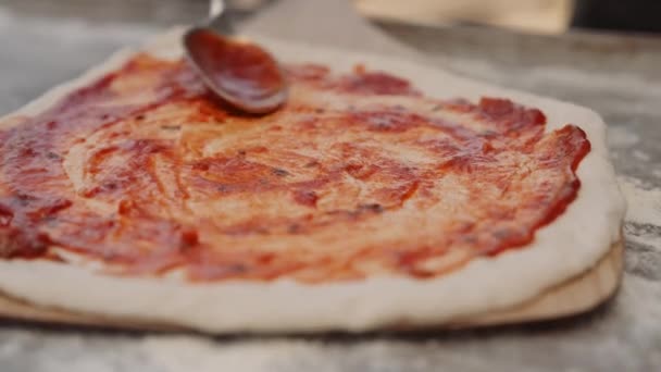 スプーンでトマトピザソースを生ピザベースに広げる男のショットを閉じる手押しのスローモーション — ストック動画