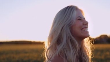 Gün batımının yumuşak ışıklarındaki buğday tarlasında güzel sarışın bir kadının portresi. Sinema Ağır Çekim Dolly Out. Kameraya Bakar ve Gülümser