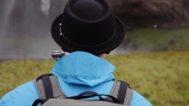 Güçlü Seljalandsfoss Şelalesi 'ni akıllı telefonuyla vuran bir erkek turistin yakın plan görüntüsü. İzlanda 'nın görkemli manzarası. Yavaş Hareket Doli Çekim