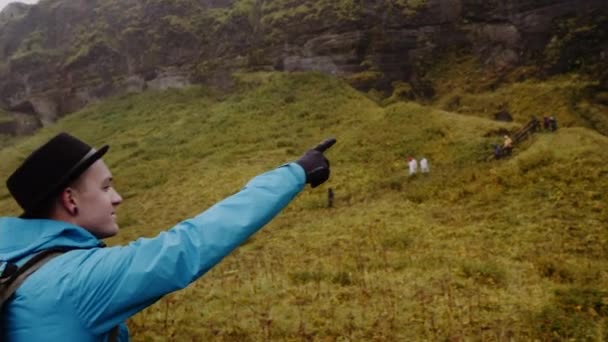 Seljalandsfoss滝の前に立つ男の観光客と彼の手でそれをポイントします 水は力で落ちる 雄大な景色 スローモーションのパンニングショット — ストック動画