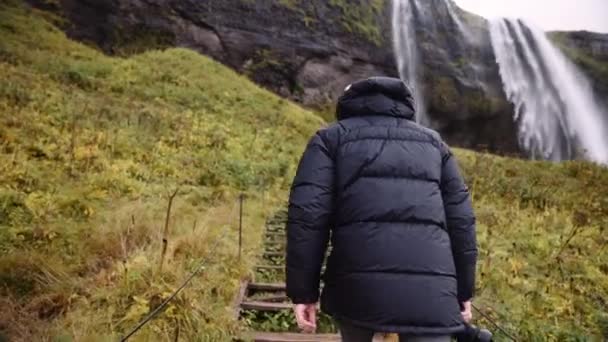 男の写真家は階段を上るSeljalandsfoss滝に向かって歩く アイスランドの雄大な景色 スローモーションショット — ストック動画