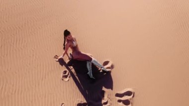 Geniş İHA Çölde Sıcak Oturan, Kum Kumu Giyen, Çizme Giyen ve Bikini Giyen Genç Kadın Üzerine Kavis Yapıyor