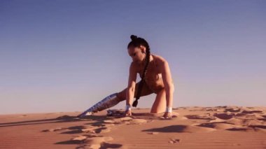 Geniş Yavaş Çekim Çölde Diz çökmüş Gümüş çizme ve Bikini giyen genç bir kadın.