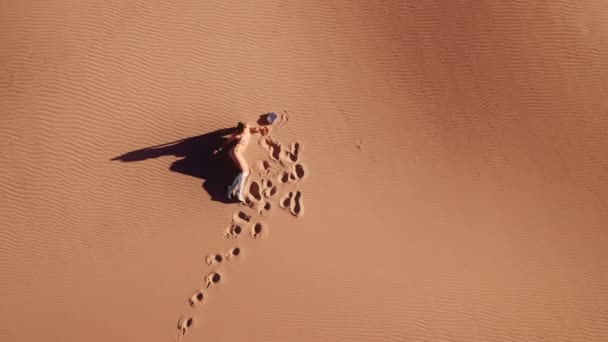 ビキニとブーツで若い女性の上にドローンは砂漠で砂に横たわっています — ストック動画