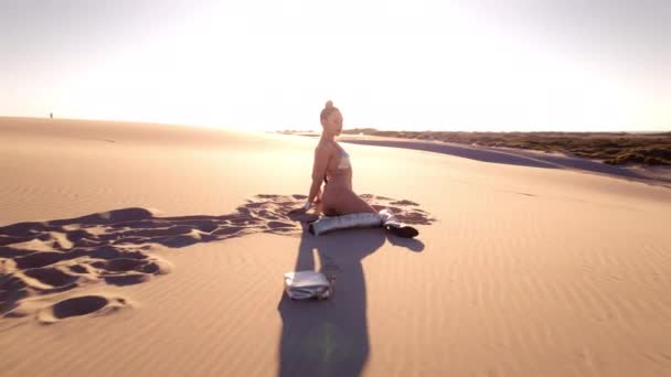 日の下砂漠の砂丘に座っているビキニとブーツの若い女性からのワイドドローンショット — ストック動画