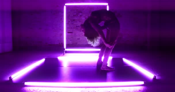 紫色の光が立ち 後ろの床に曲げ彼女の後ろに触れることによって囲まれた女性のコンストラクショニストのロックダウンワイドショット — ストック動画