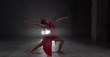 Baştan Çıkarıcı Kırmızı Elbiseli Genç Dansçı Karanlık Stüdyoda Sahne Işıklarına Karşı Çıplak Ayakla Sahne alıyor. Yağmur yağışını taklit ederek yere düşen su damlaları. Çekim dışı Dolly