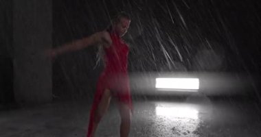 Baştan Çıkarıcı Kırmızı Elbiseli Genç Dansçı Karanlık Stüdyoda Sahne Işıklarına Karşı Çıplak Ayakla Sahne alıyor. Yağmur yağışını taklit ederek yere düşen su damlaları. Sol ve Sağ Görüntü Yayılıyor