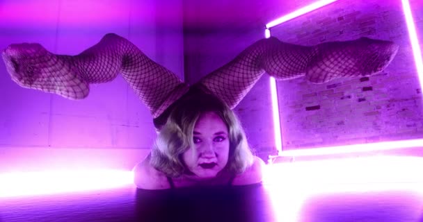紫色の光に囲まれた女性コンストロールのワイドショットをフロントに寝そべって彼女の後ろに彼女のストレッチ足を返す — ストック動画