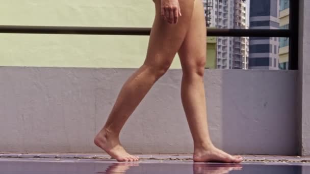都市の屋上にインフィニティプールの端に沿って歩く若い裸足の女性の動きの遅いショットを追跡 — ストック動画