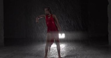 Baştan Çıkarıcı Kırmızı Elbiseli Genç Dansçı Karanlık Stüdyoda Sahne Işıklarına Karşı Çıplak Ayakla Sahne alıyor. Yere düşen su damlaları Yağmur Sağanağını taklit ediyor