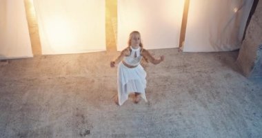 Beyaz Elbiseli Uzun Sarı Saçlı Zarif Genç Dansçı Beyaz Arkaplan ve Sahne Işıklarına Karşı Stüdyoda Sahne Açılıyor. Slow Motion Top View Shot. Kamera Kadını İzliyor