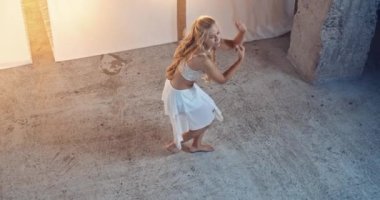 Beyaz Elbiseli Uzun Sarı Saçlı Zarif Genç Dansçı Beyaz Arkaplan ve Sahne Işıklarına Karşı Stüdyoda Sahne Açılıyor. Slow Motion Top View Shot. Kamera Kadını İzliyor