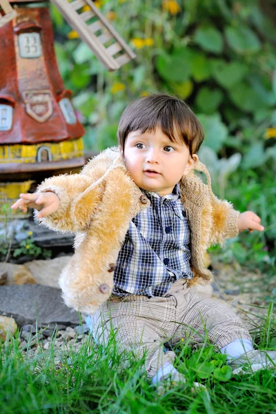 Bebê bonito sentado na grama ao ar livre em jaqueta de outono — Fotografia de Stock