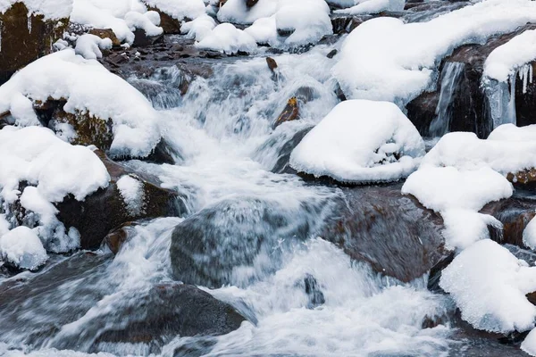 Pequeña cascada de agua fría fluye entre las piedras cubiertas de nieve — Foto de Stock