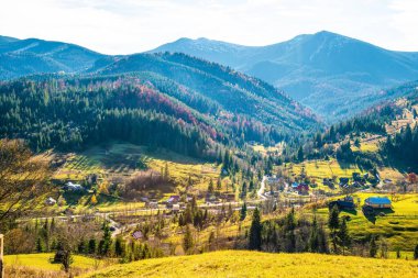Karpat dağlarını kaplayan güzel renkli ormanlar ve sıcak sonbahar gökyüzünün arka planında küçük bir köy.