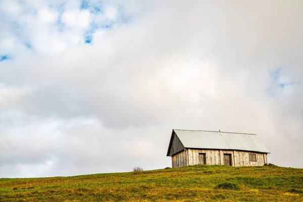 A lonely little gray house stands on a fresh wet green meadow amidst a dense gray fog