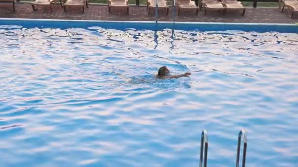 Mujer nada en una piscina con agua clara en el fondo de una puesta de sol de verano en vacaciones — Vídeo de stock