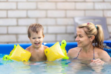 Annem havuzda kolsuz çıplak bir bebekle oynuyor yaz günbatımının arka planında.