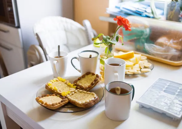 Desayuno con té y café, trozos de fruta, tostadas con mantequilla y nueces en la mesa en la cocina por la mañana — Foto de Stock