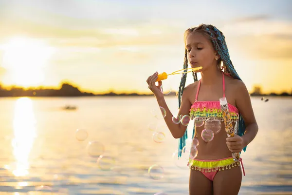 Mädchen mit afrikanischen Zöpfen im Badeanzug bläst im Sommerurlaub Seifenblasen — Stockfoto