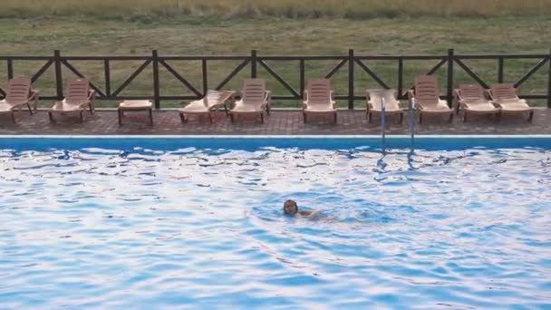 Kvinnen svømmer i et basseng med klart vann i bakgrunnen av en sommersolnedgang på ferie. – stockvideo