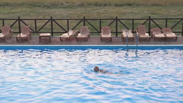 Mujer nada en una piscina con agua clara en el fondo de una puesta de sol de verano en vacaciones — Vídeo de stock