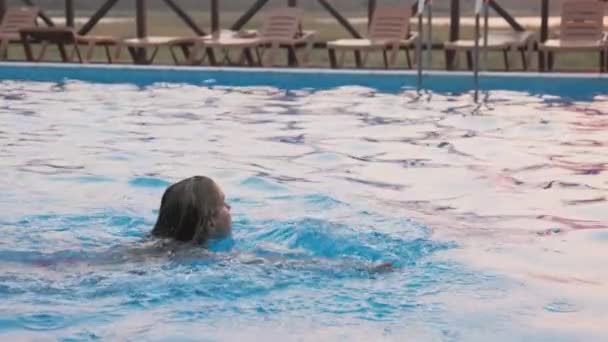 女性は休暇中の夏の日没を背景に澄んだ水でプールで泳ぐ — ストック動画