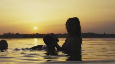 Annem gölde kolsuz çıplak bir bebekle oynuyor yaz günbatımının arka planında.