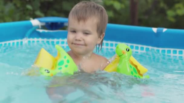 Ребенок в рукавах плавает в бассейне во дворе — стоковое видео