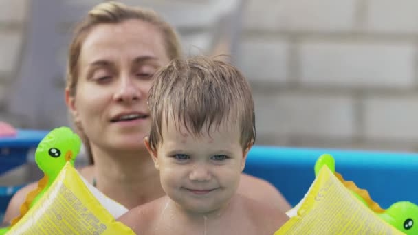 Mãe brinca com um bebê nu em subidas na piscina contra o fundo de um pôr do sol de verão — Vídeo de Stock