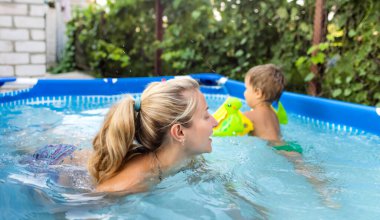 Annem havuzda kolsuz çıplak bir bebekle oynuyor yaz günbatımının arka planında.