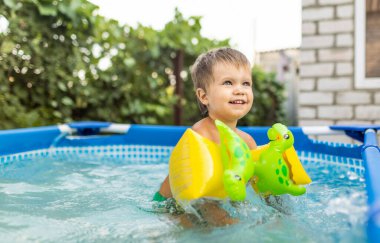 Üst kollu çocuk bahçedeki havuzda yüzüyor.