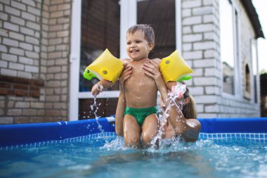 Annem havuzda kolsuz çıplak bir bebekle oynuyor yaz günbatımının arka planında.