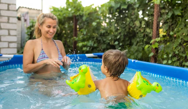 Mom plays with a naked baby in oversleeves in the pool against the background of a summer sunset — Stock Photo, Image