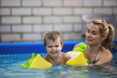 Annem havuzda kolsuz çıplak bir bebekle oynuyor yaz günbatımının arka planında.